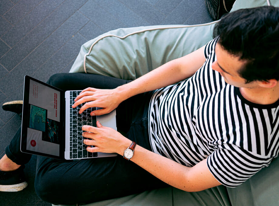 A teenager sits and uses a small laptop computer.