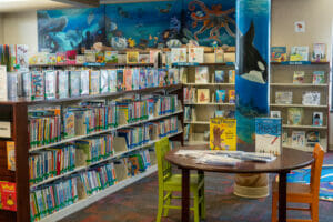 The children's department at the Lexington library that shows the ocean mural on the wall and stacks of children's books with displays.