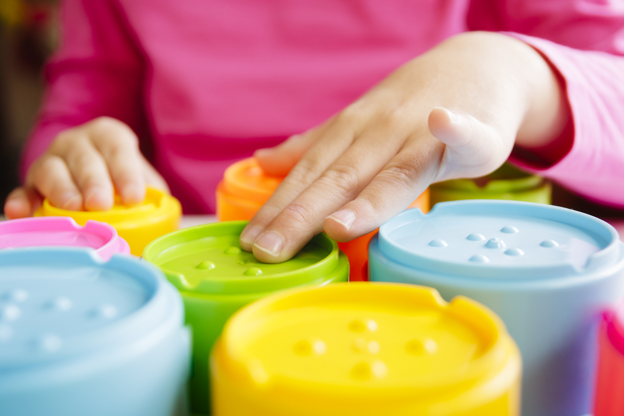 Hands of a child with poor vision touching the colorful tactile toy cups as a part of occupational therapy.