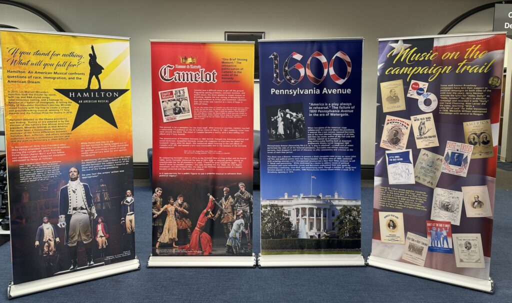 Four, multicolored pull-up banners with information about the Hamilton musical and campaign songs.